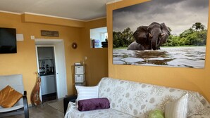 Un salon avec un canapé, une couverture verte et un coussin. Il y a un tableau représentant un éléphant accroché au mur.