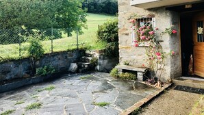 Une terrasse en pierre avec un muret en pierre, un petit banc et une jardinière ornée de fleurs roses.