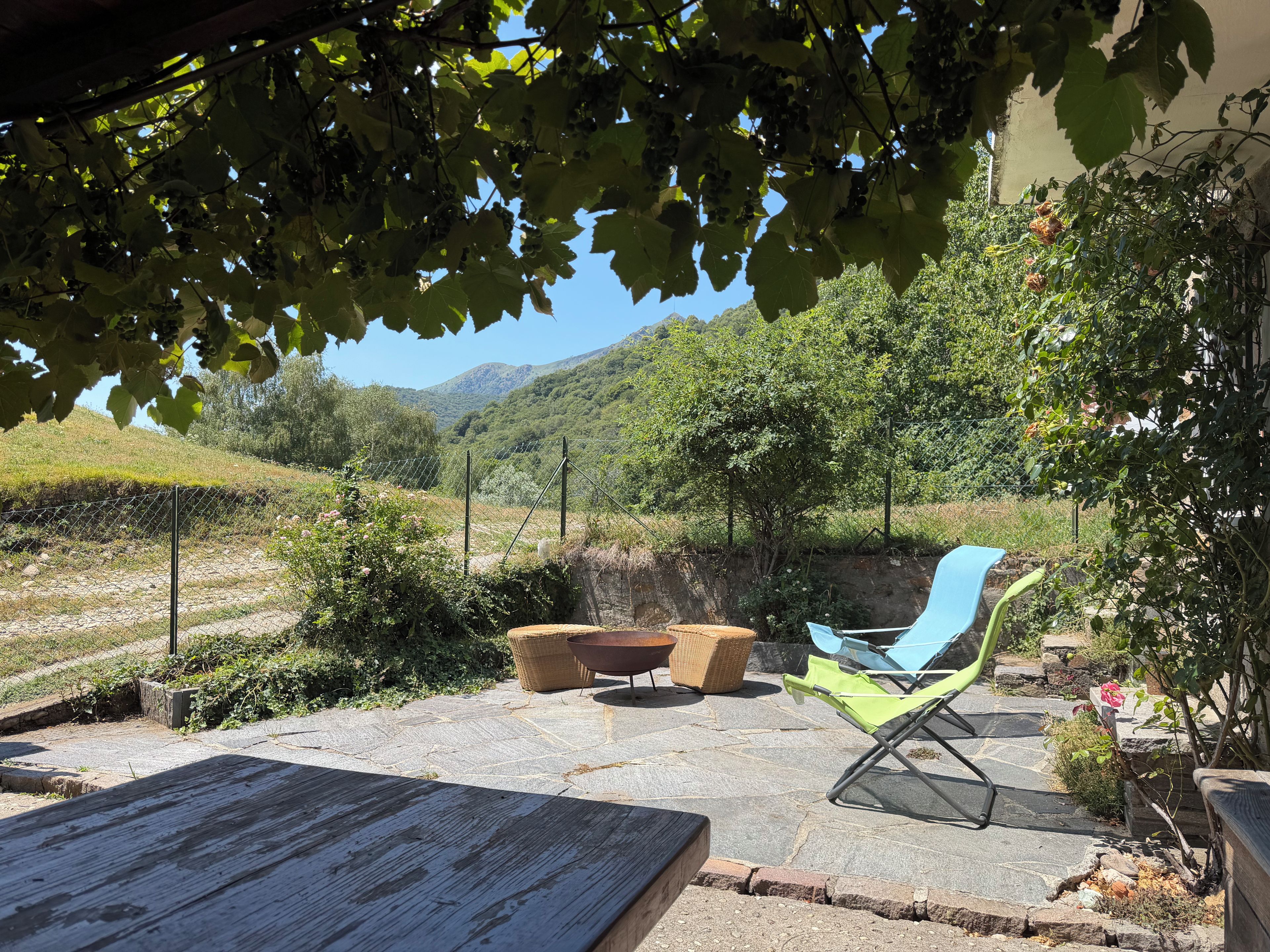 Um pátio externo com mesa, cadeiras e vista para vinhedos e colinas.