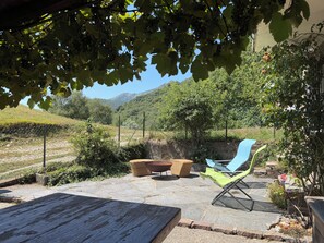 Une terrasse extérieure avec une table, des chaises et une vue sur un vignoble et des collines.