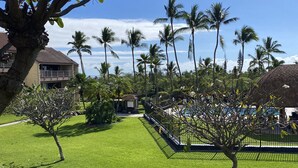 A well-maintained lawn with a few trees, a fenced pool area, and a building with a balcony in the background. - Newly Renovated Condo with SUP Paddle Boards and Golf Clubs Included (Kailua-Kona)