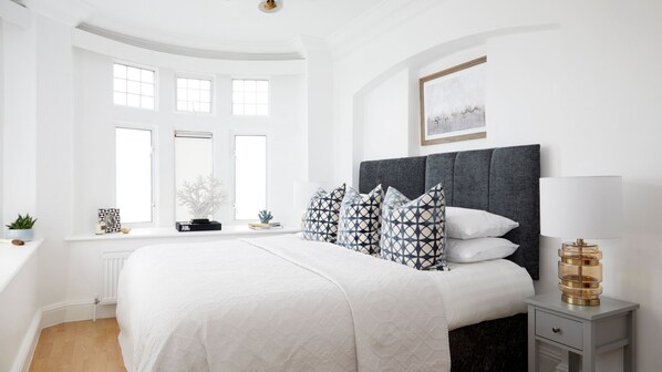 A modern bedroom with a large bed, a bedside table, a lamp, and a window with multiple panes.