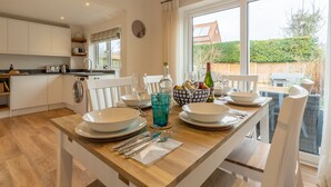 Una cocina moderna con armarios blancos, encimera de madera y comedor con sillas blancas y una mesa de madera lista para una comida.