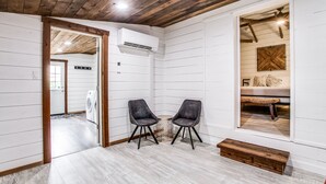 A room with a wooden ceiling, white walls, and a wooden floor. There are two chairs, a bench, and a small table. - The Blue Cactus in Downtown McKinney (Mckinney)