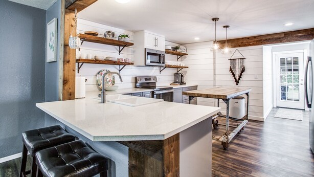 A modern kitchen with a central island, wooden beams, white cabinetry, and a microwave. - The Blue Cactus in Downtown McKinney (Mckinney)