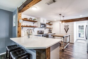 A modern kitchen with a central island, wooden beams, white cabinetry, and a microwave. - The Blue Cactus in Downtown McKinney (Mckinney)