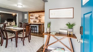 A dining area with a wooden table and chairs, a kitchen in the background, and a blue door with a 'WELCOME' sign. - The Blue Cactus in Downtown McKinney (Mckinney)