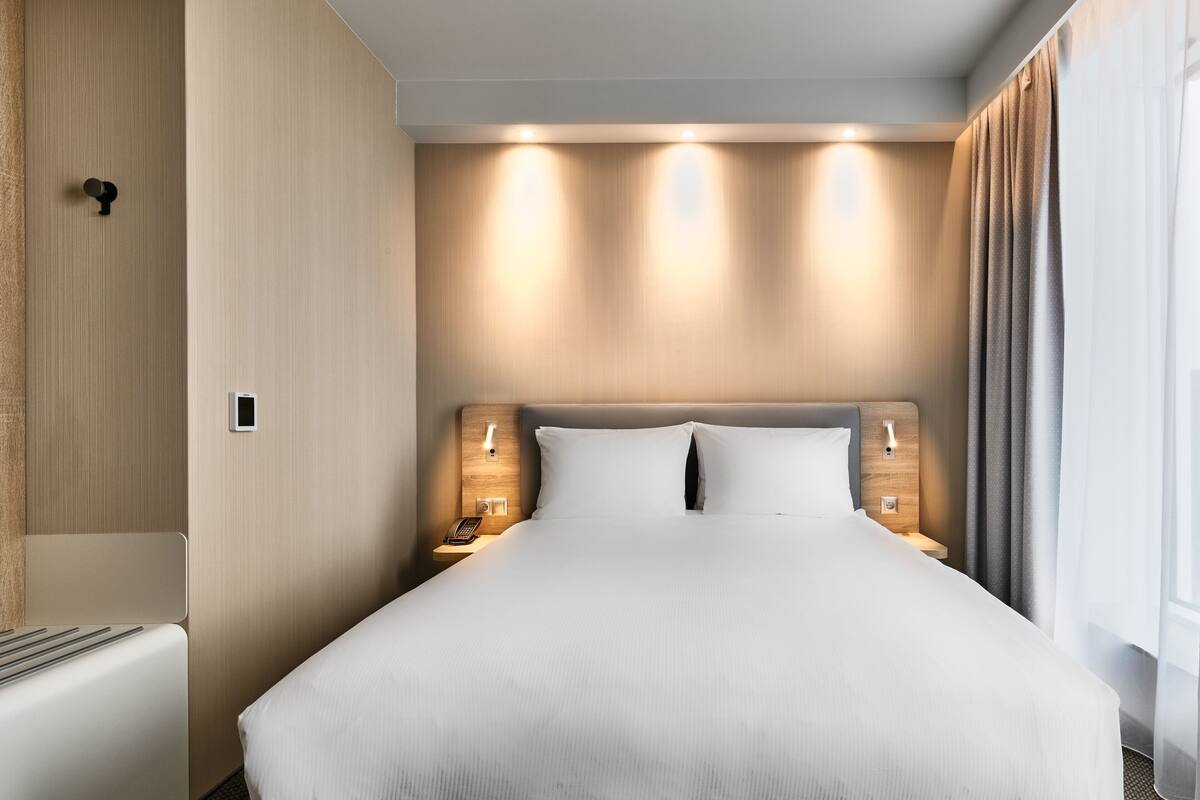 A modern hotel room with a large bed, bedside lamps, and a wooden headboard.