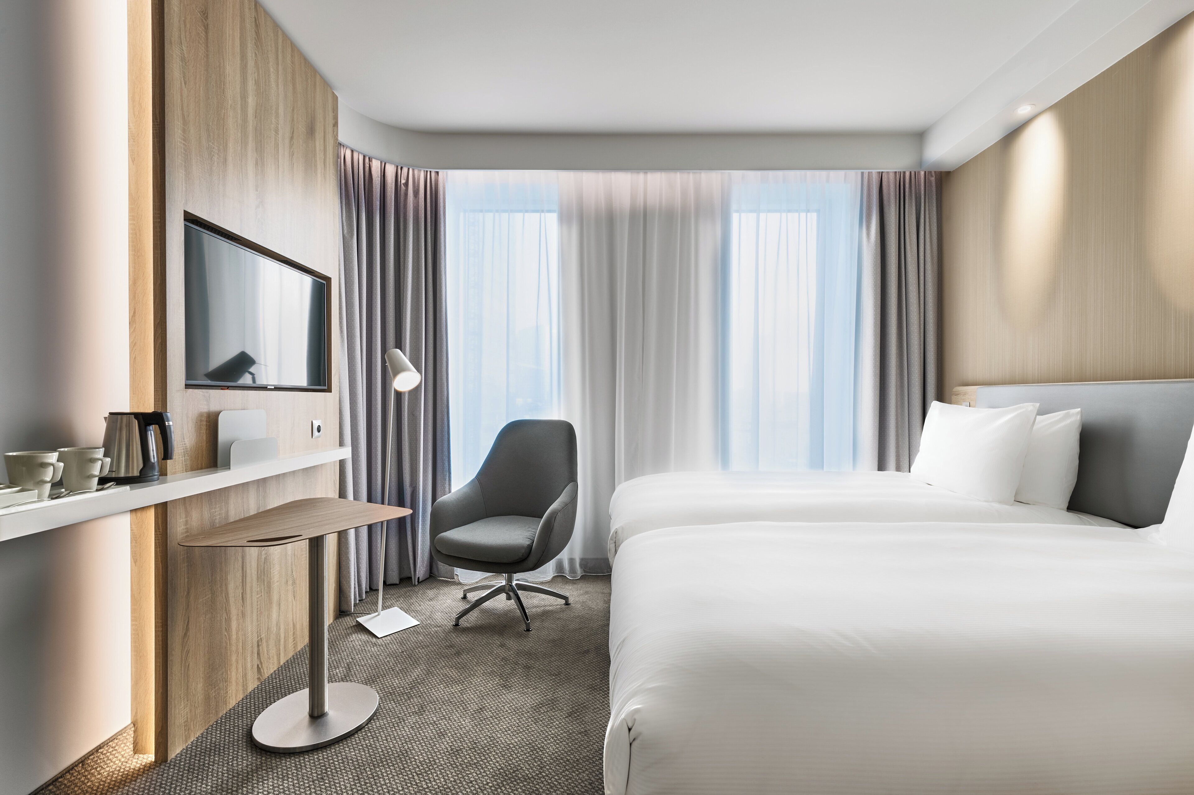 Hotellihuone, jossa on sänky, työpöytä tuolilla, televisio ja ikkuna, jossa on verhot.