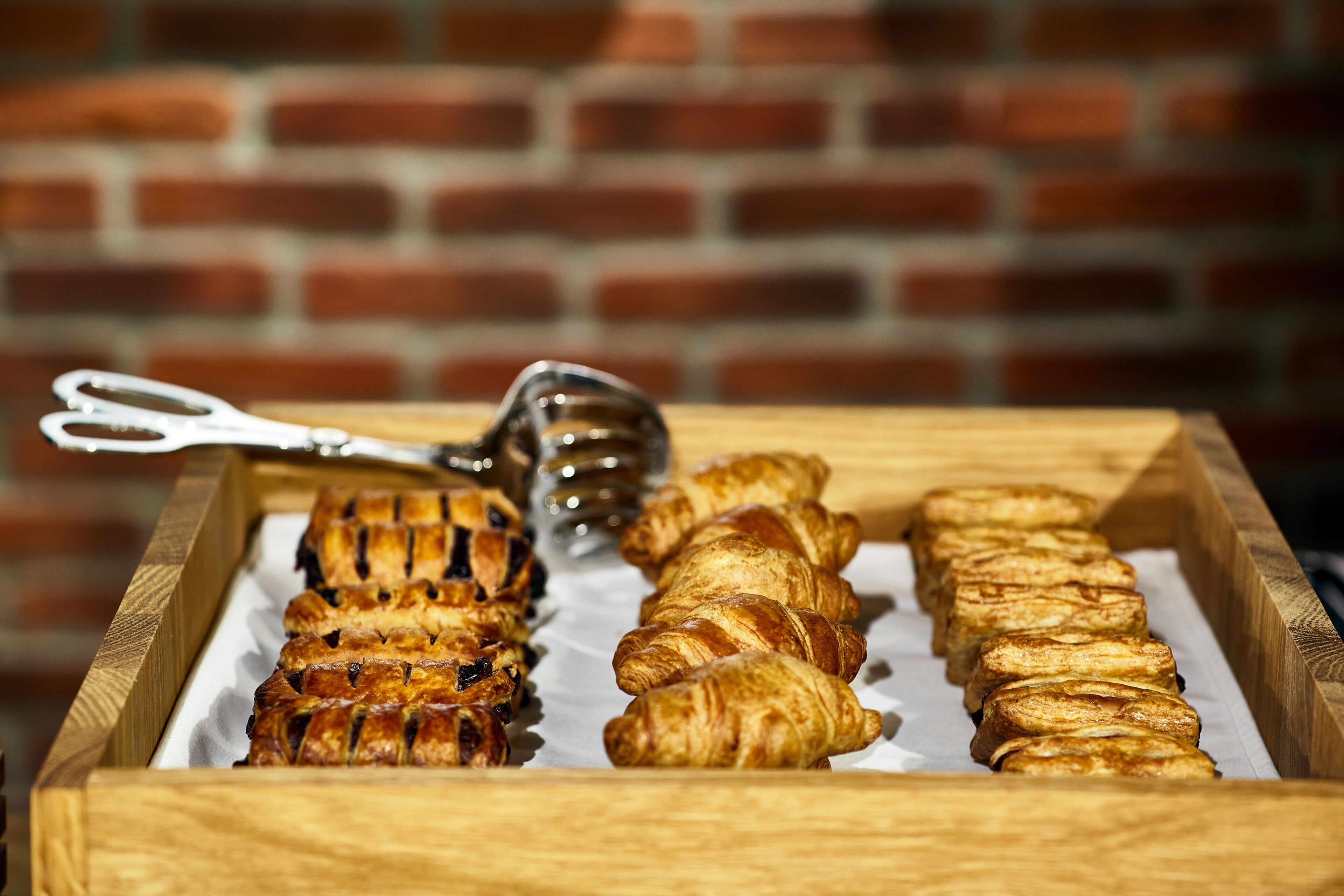 Een houten dienblad met verschillende gebakjes, waaronder croissants en een taart, met een schaar en een honinglepel erbovenop.