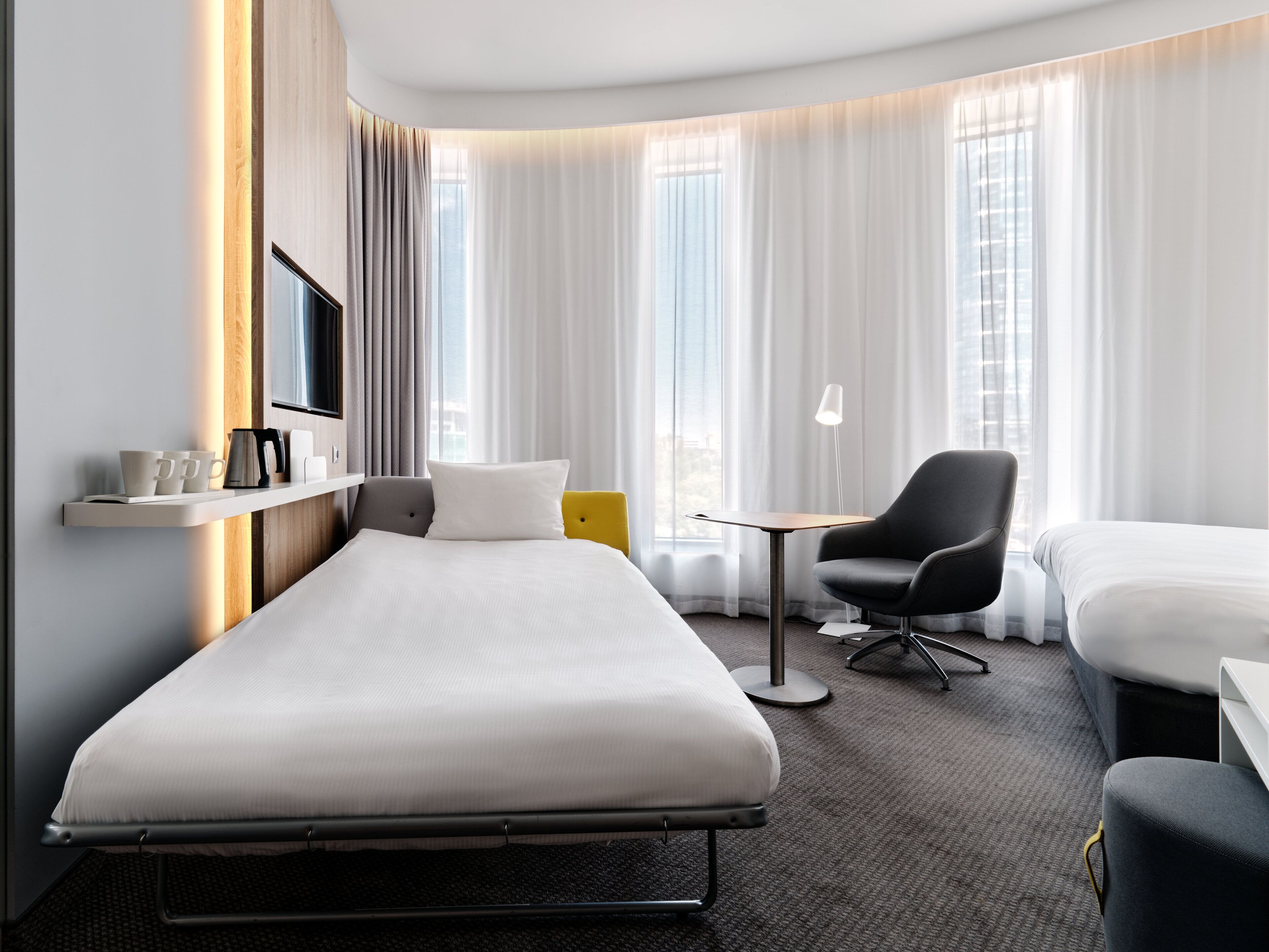 A hotel room with a single bed, a small desk, a chair, and a TV mounted on the wall.