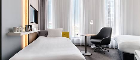 A hotel room with a single bed, a small desk, a chair, and a TV mounted on the wall.