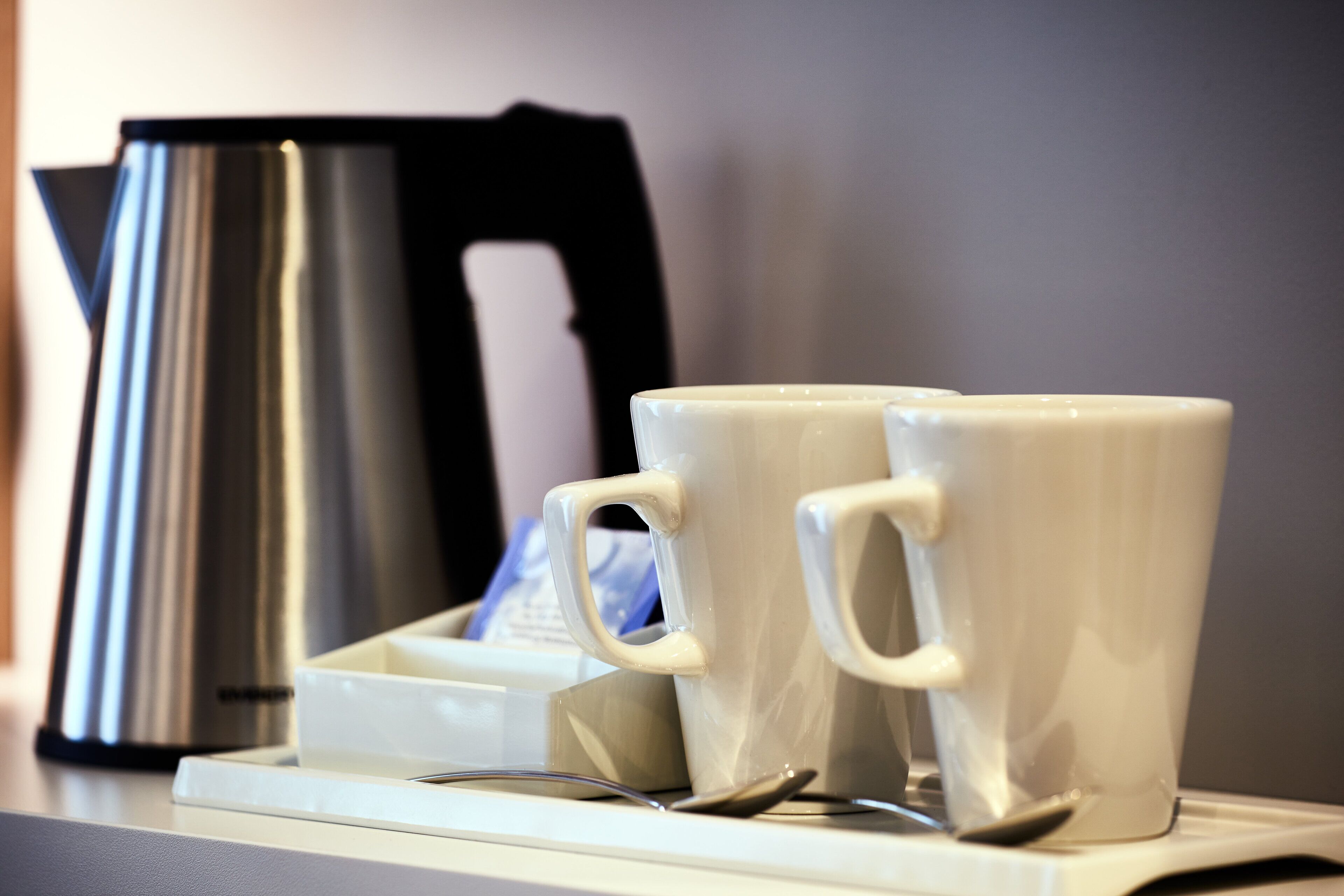 Duas chávenas de cerâmica branca sobre um serviço de chá, com uma colher, uma cafeteira preta e um recipiente branco ao fundo.