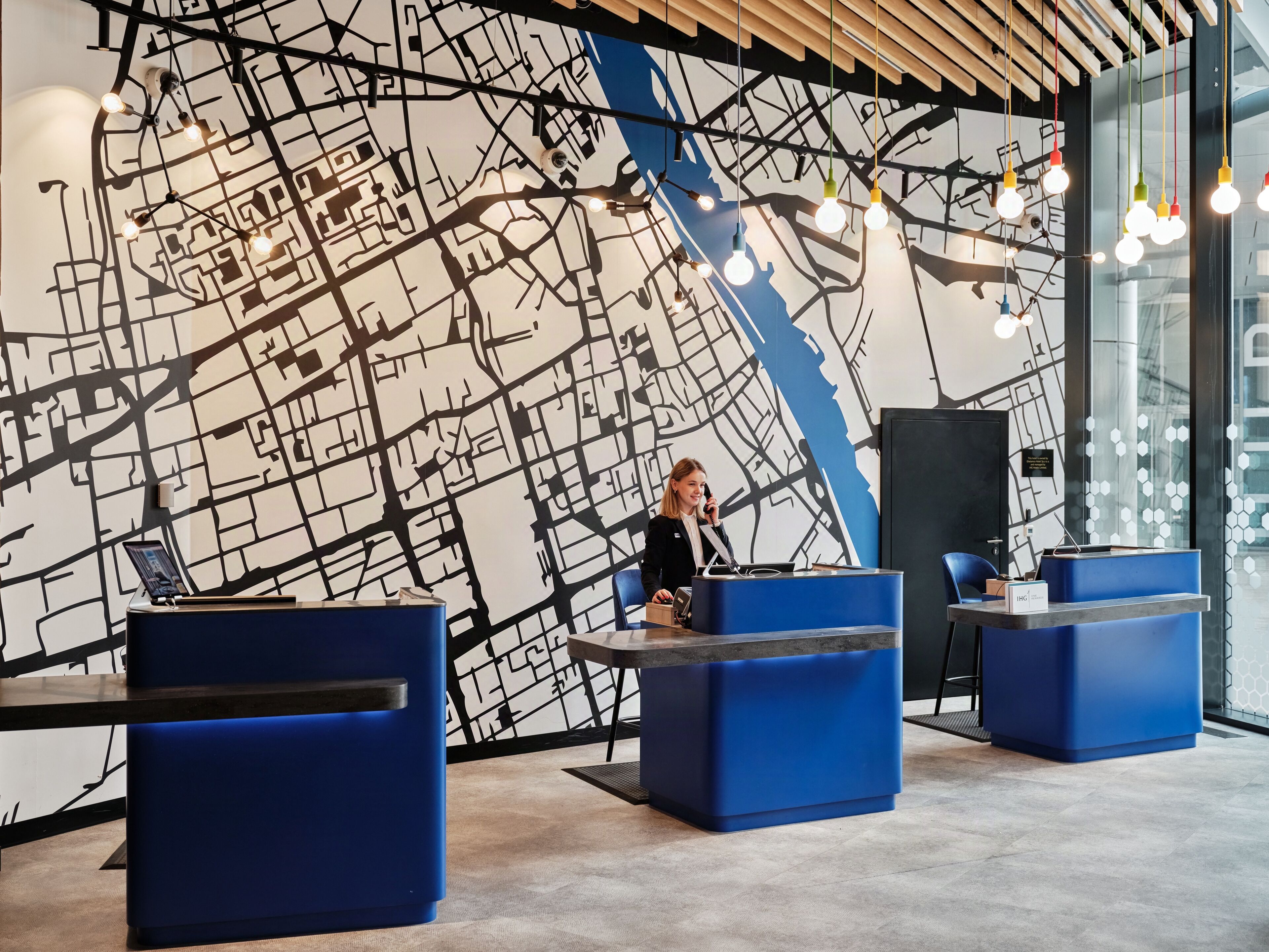 Un área de recepción moderna con un mural grande de mapa blanco y negro, asientos azules y lámparas colgantes.