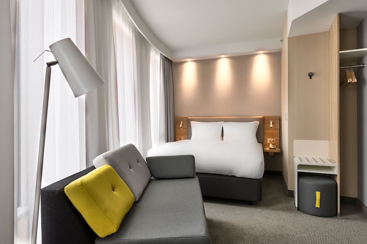 A modern hotel room with a bed, a sofa, a desk, and a wardrobe.
