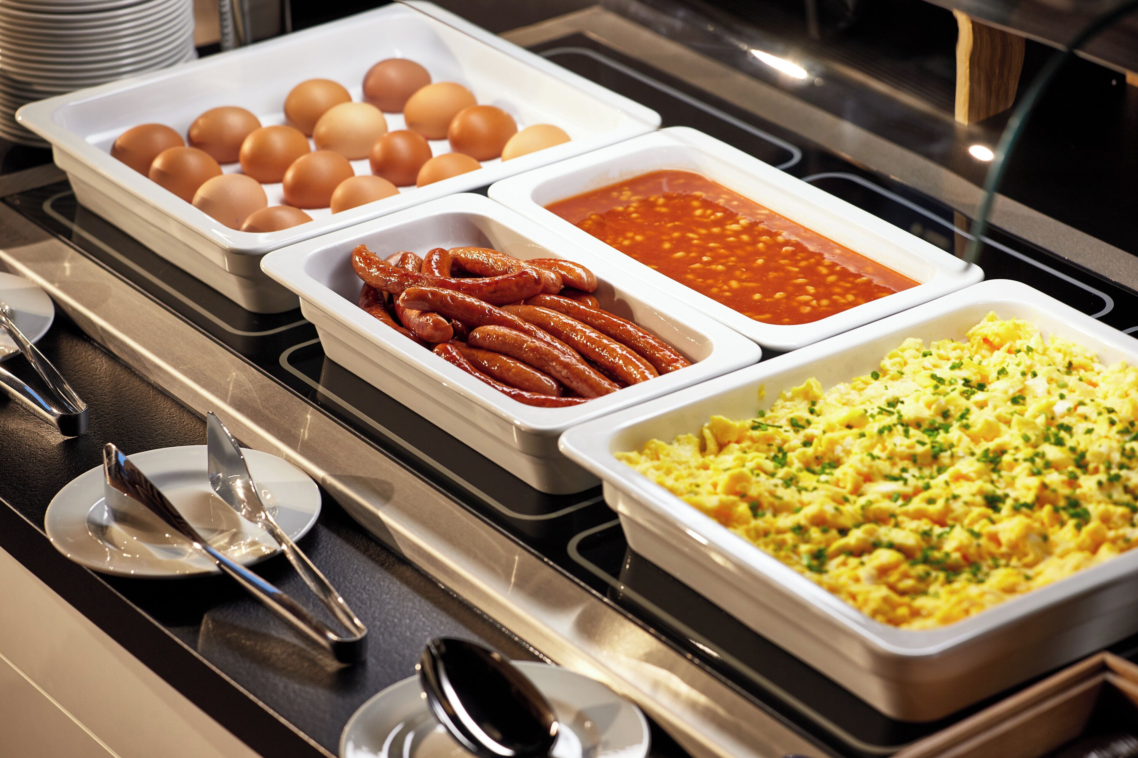 A buffet with various food options including eggs, sausages, beans, and scrambled eggs.