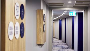 Un couloir d’hôtel avec des panneaux de signalisation au mur, un panneau décoratif en bois et un tapis à motifs.