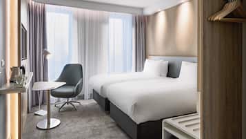 Una habitación de hotel con cama, escritorio, silla y ventana con cortinas.