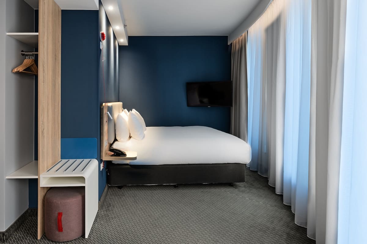 A modern hotel room with a bed, a TV, a desk, and a wardrobe.
