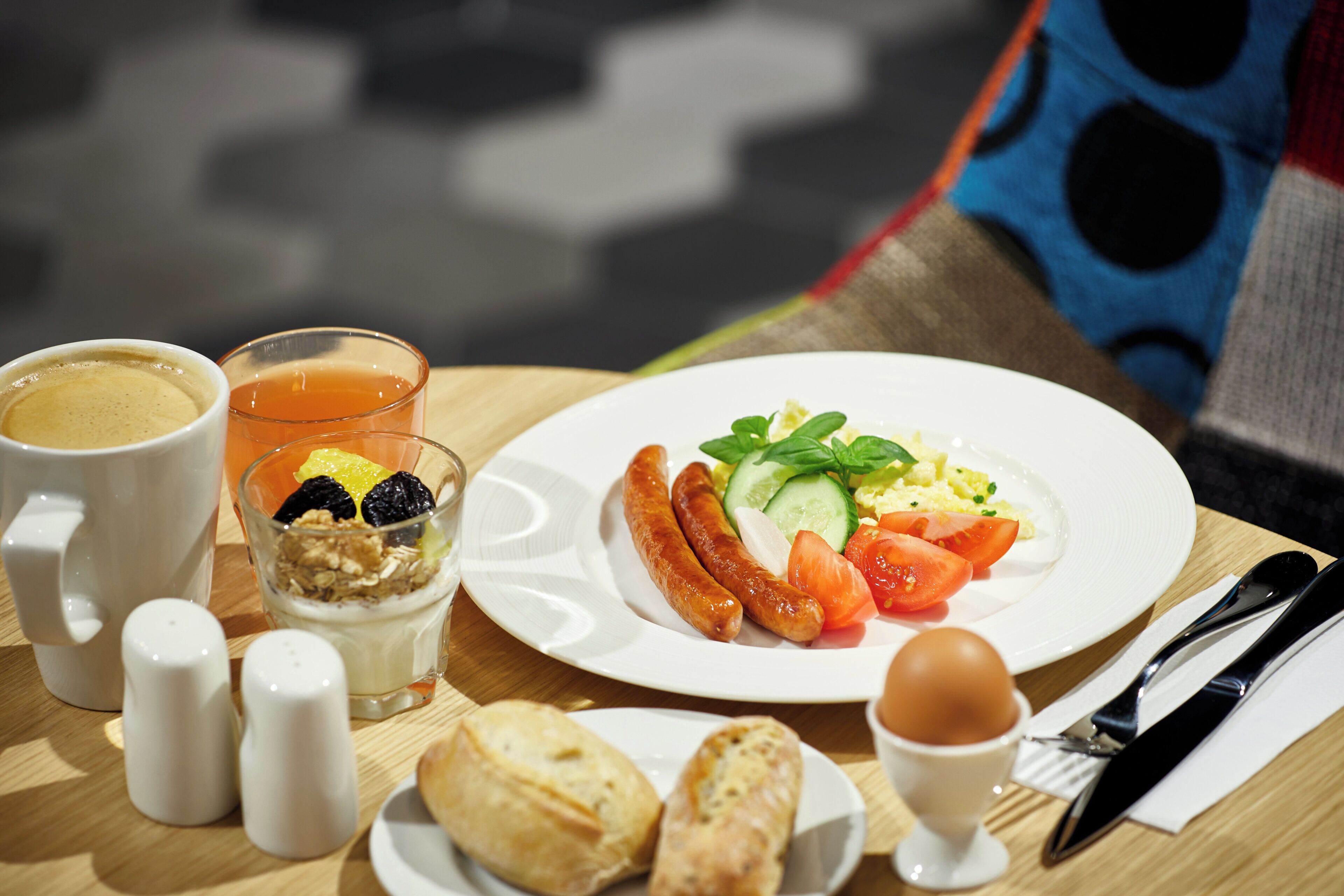 A breakfast setting with a plate of food, a cup of coffee, a glass of juice, and a napkin with cutlery.