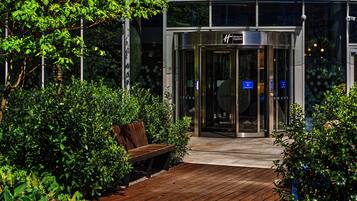A Holiday Inn Express entrance with a glass door, surrounded by greenery and a wooden deck.