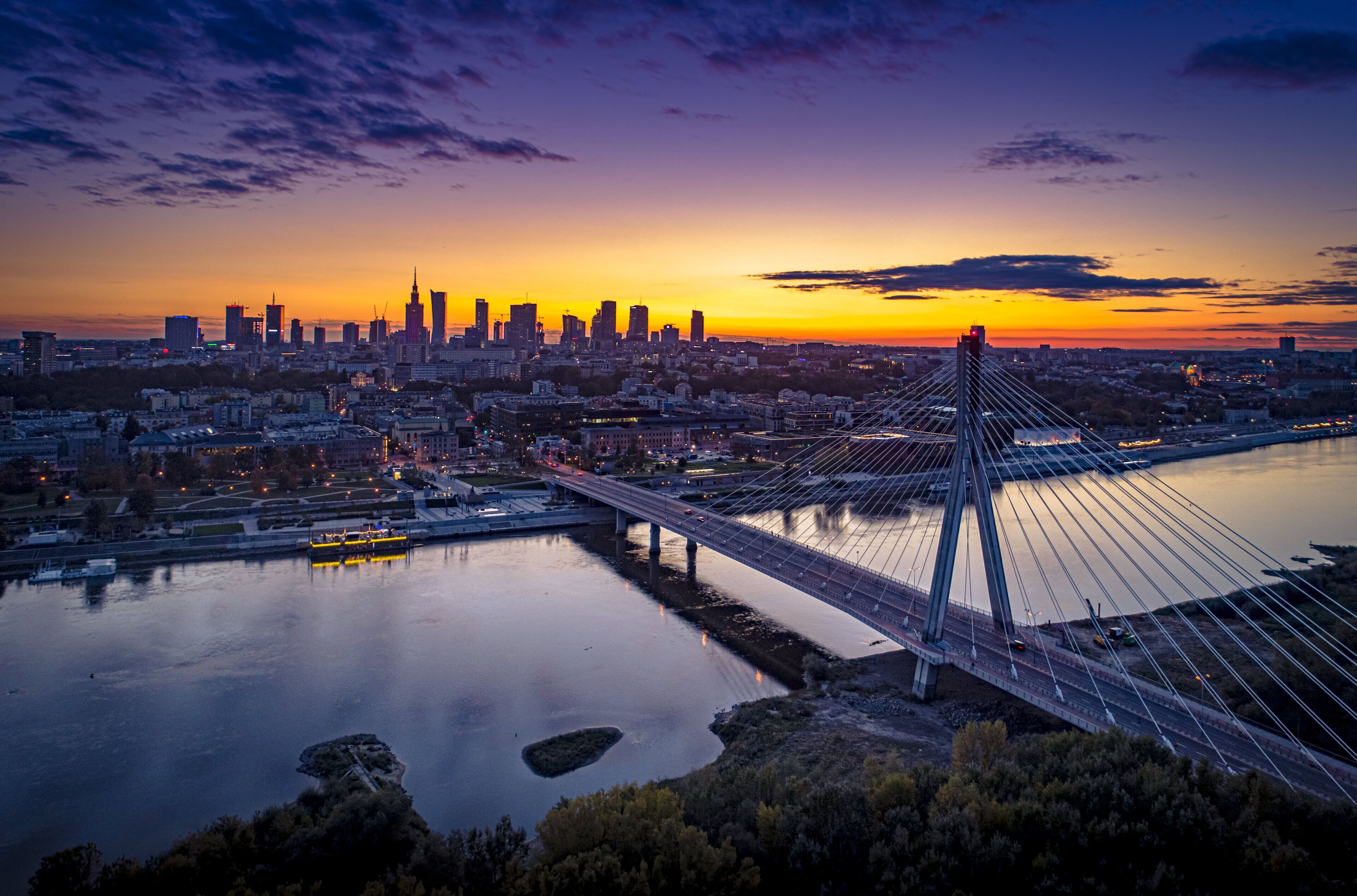 A city skyline at sunset with a prominent bridge spanning a river.