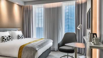 A modern hotel room with a large bed, a desk, and a chair.