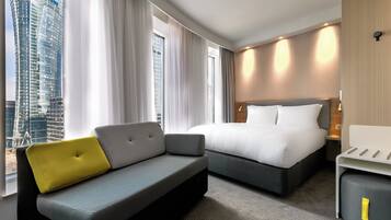 A hotel room with a bed, a sofa, a small table, and a view of a cityscape.