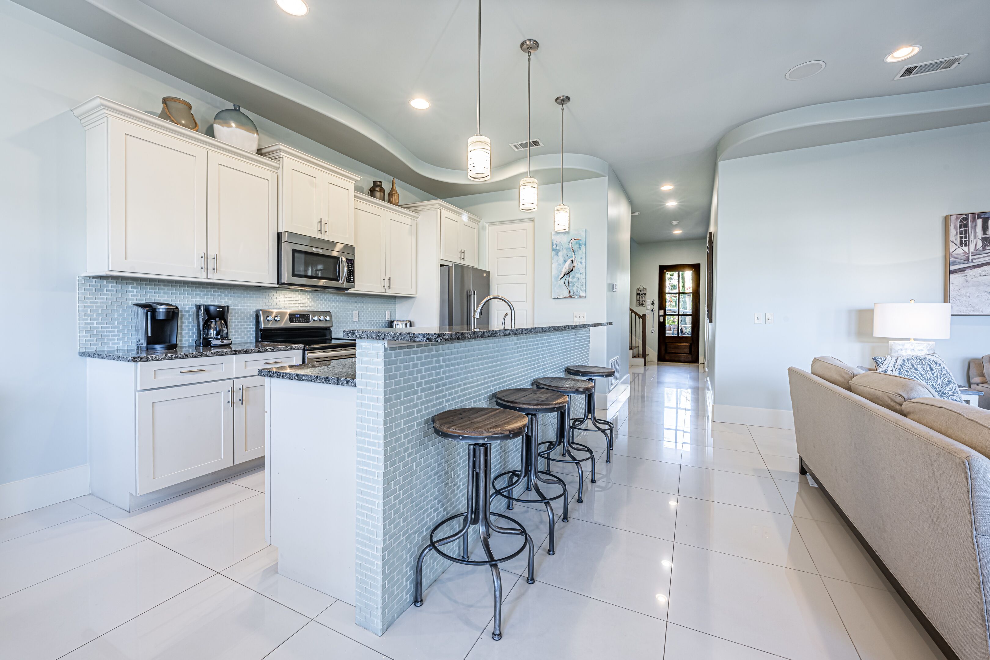 A modern kitchen with white cabinets, a central island with stools, stainless steel appliances, and pendant lighting.