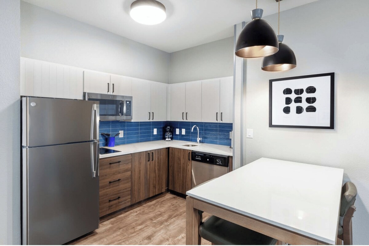 A modern kitchen with stainless steel appliances, wooden cabinets, and a blue tiled backsplash.