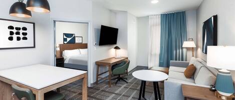 A hotel room with a dining area, a sofa, a TV, and a patterned rug.