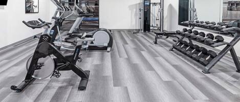 A gym with treadmills, stationary bikes, a rowing machine, and a rack of dumbbells.