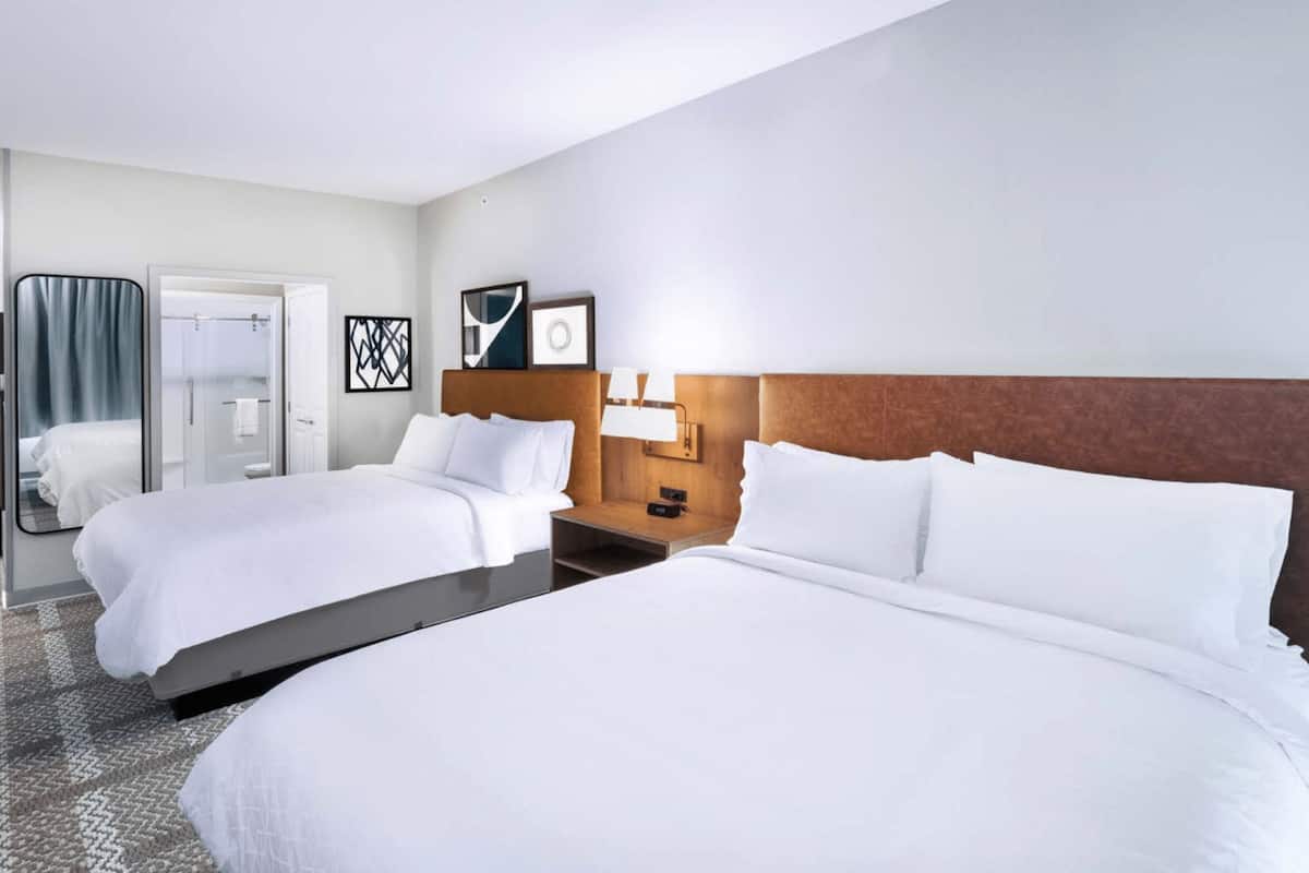 A hotel room with two beds, a wooden headboard, a nightstand with a lamp, and a framed picture on the wall.