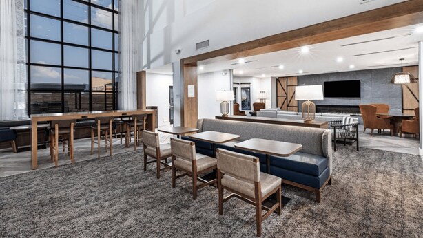 A spacious hotel lobby with a large window, a seating area with sofas and tables, and a flat-screen TV mounted on the wall. - Staybridge Suites Waco South - Woodway by IHG (Waco)