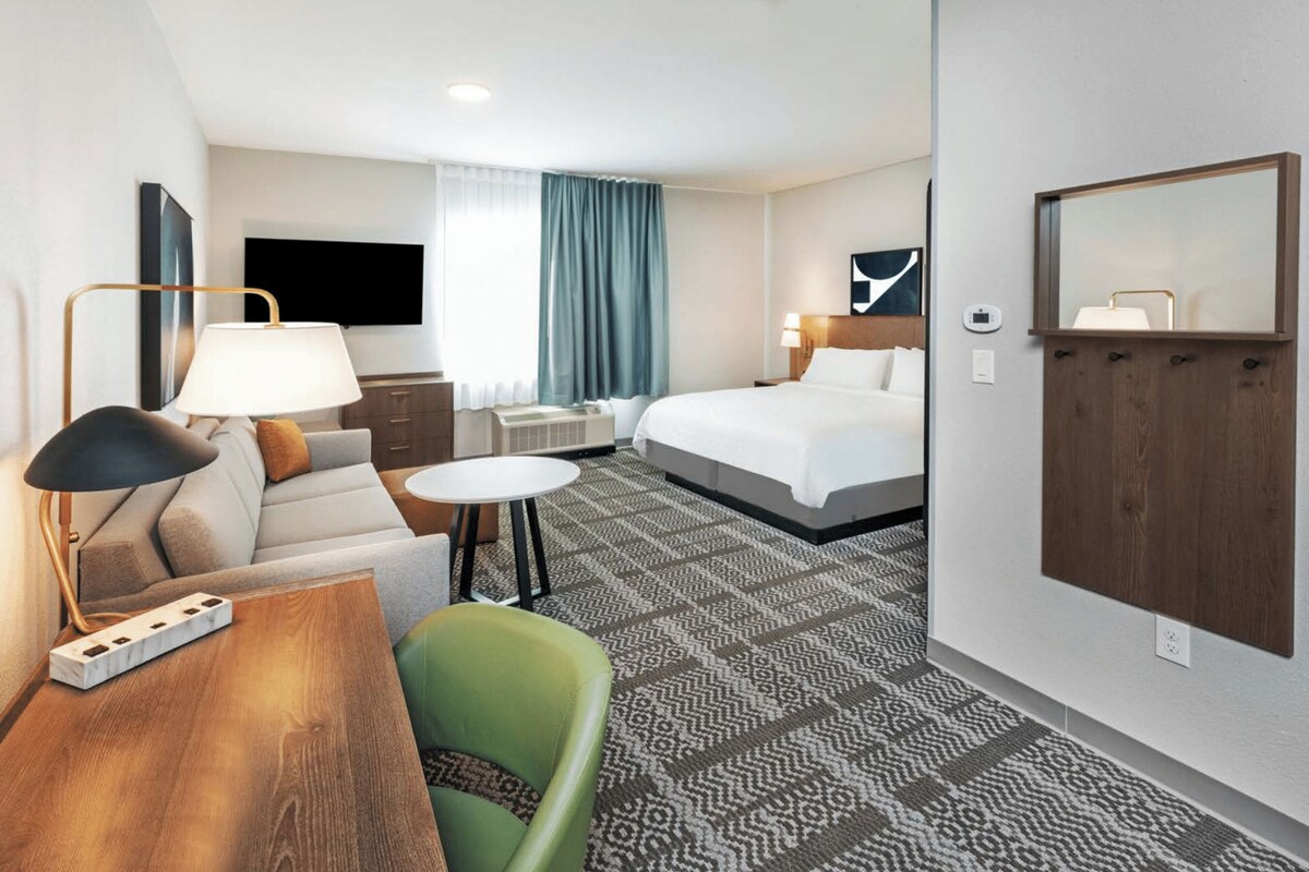 A hotel room with a bed, a sofa, a desk, a chair, a TV, and a mirror.