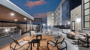 An outdoor patio with a grill, seating, and a pool in the background. - Staybridge Suites Waco South - Woodway by IHG (Waco)