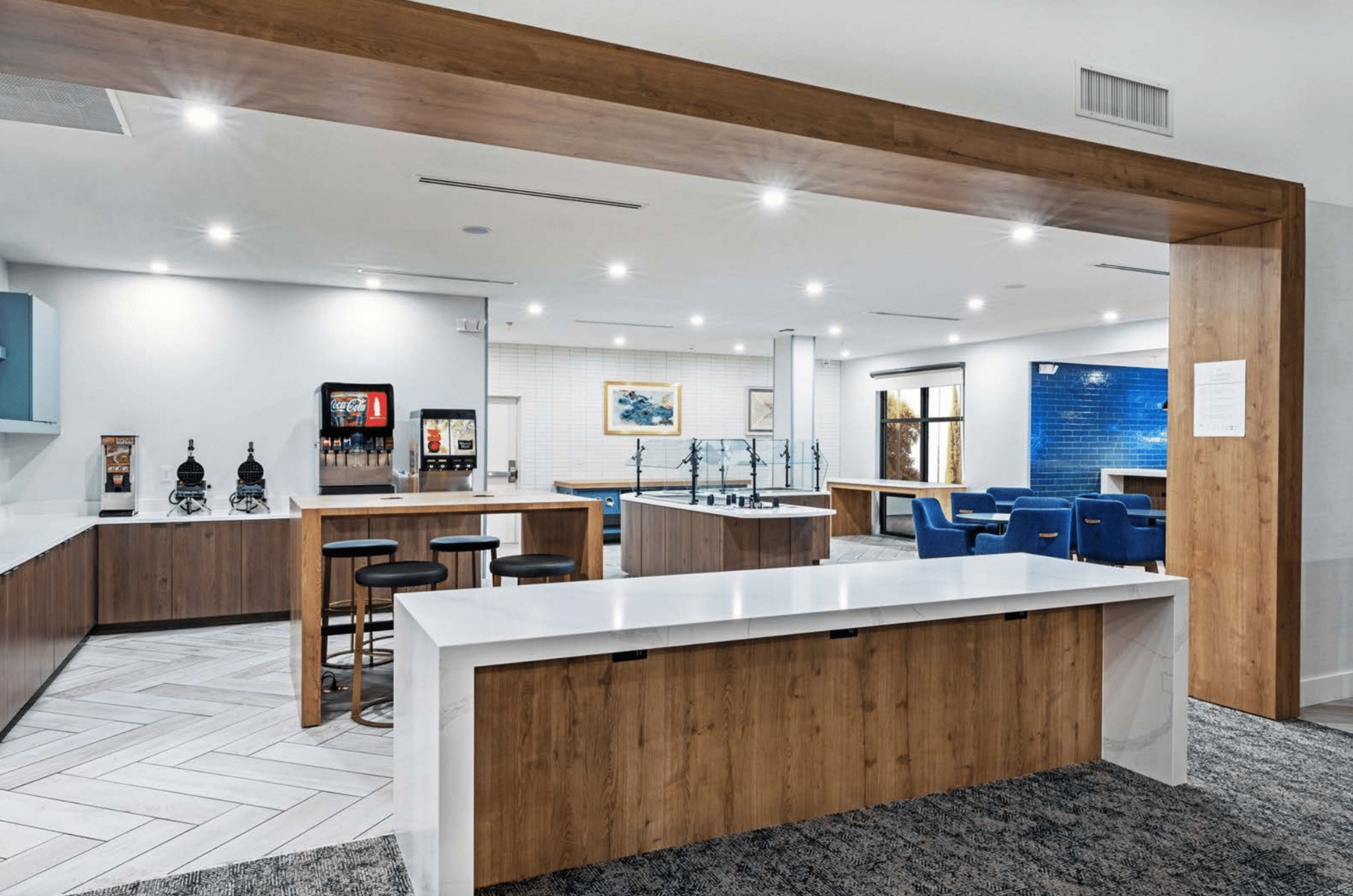 A modern kitchen with a central island, bar stools, and a seating area with blue chairs.