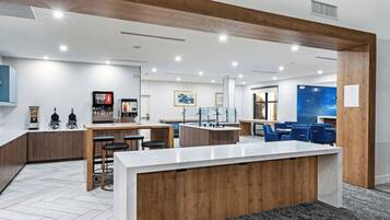 A modern kitchen with a central island, bar stools, and a seating area with blue chairs.