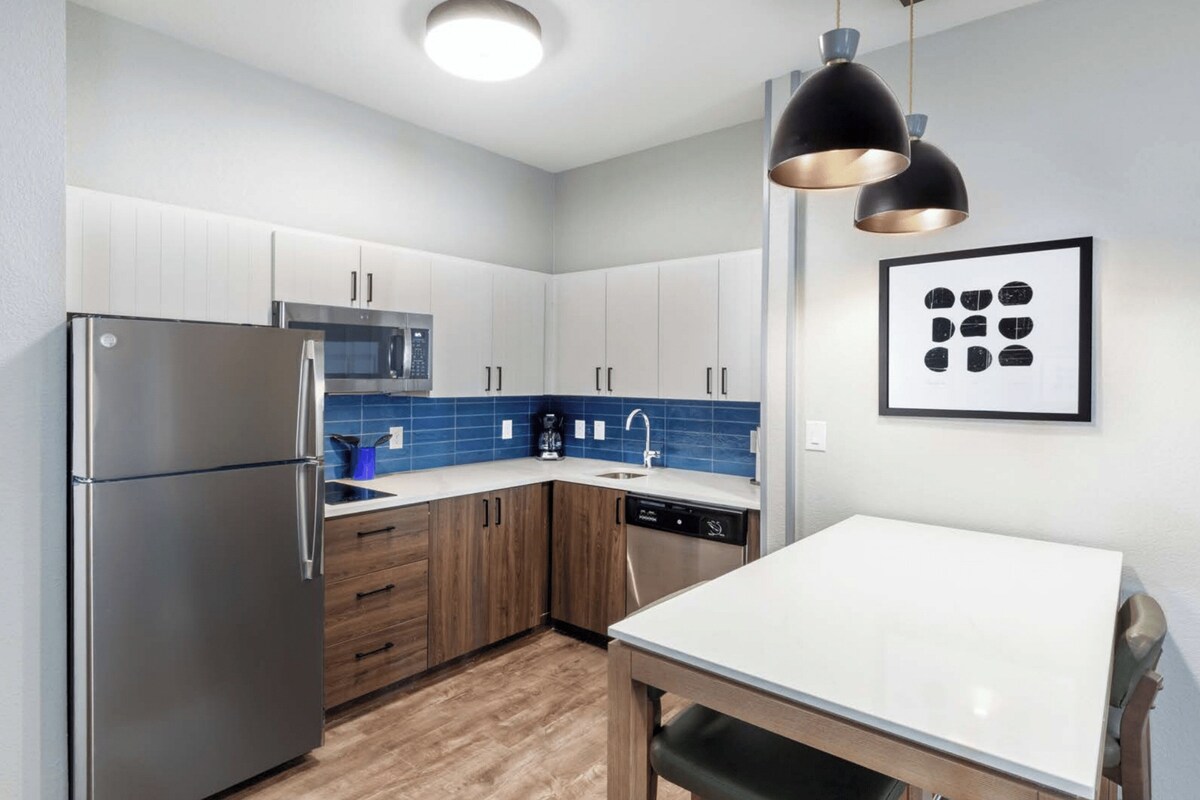 A modern kitchen with stainless steel appliances, wooden cabinets, and a blue tiled backsplash.