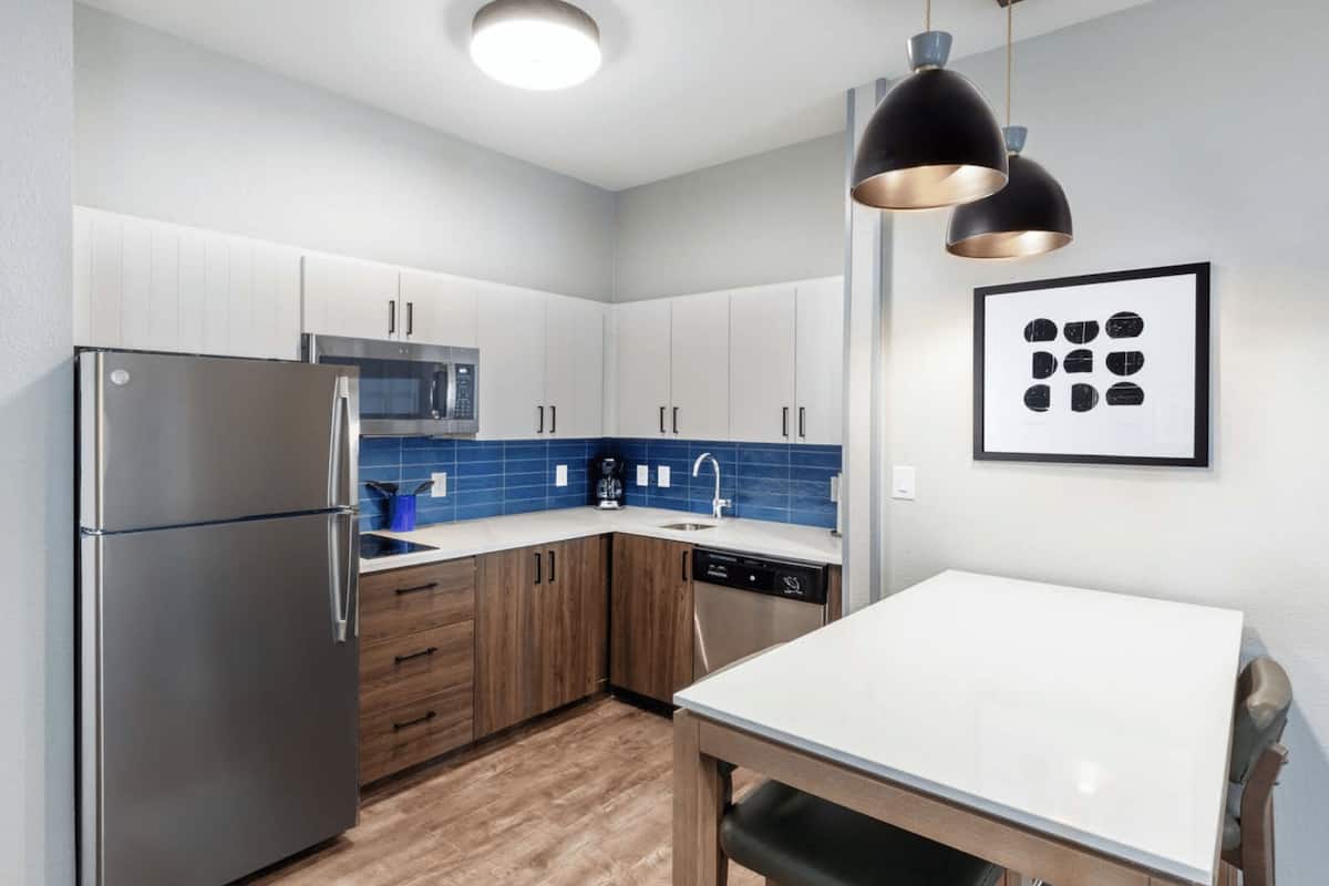 A modern kitchen with stainless steel appliances, wooden cabinets, and a blue tiled backsplash.