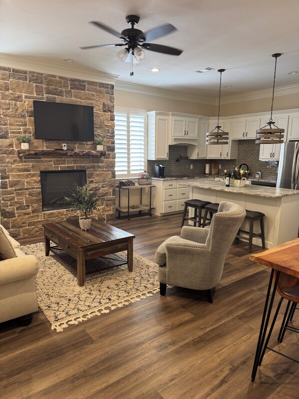 A modern kitchen with white cabinets, a stone accent wall, a built-in oven, and a large island with bar stools.
