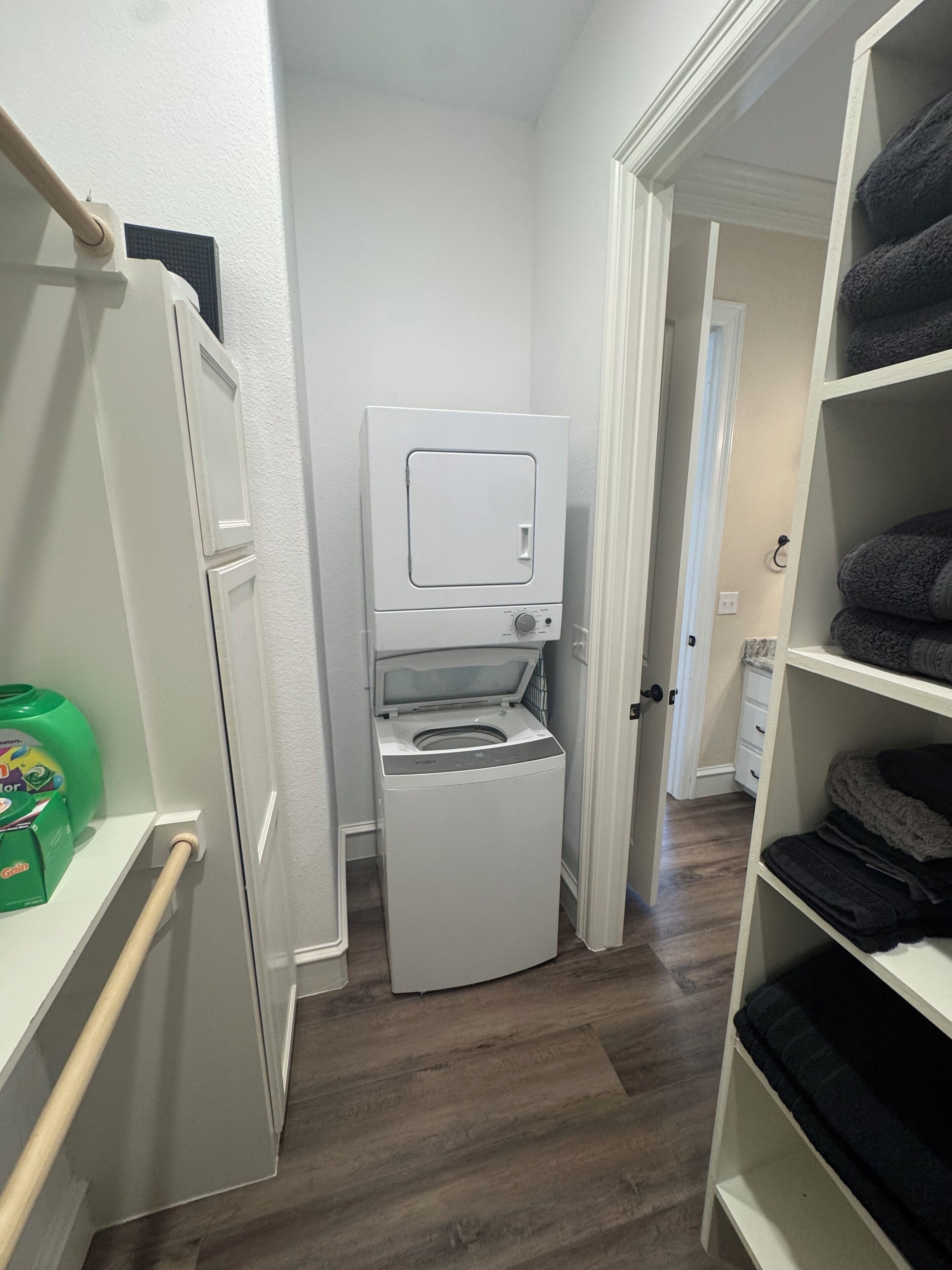 Un cuarto de lavandería con lavadora y secadora de carga frontal, un estante con toallas dobladas y una botella de detergente verde.