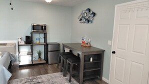 A compact kitchen with a microwave, refrigerator, and a small dining area with stools. - Lou's Place @ COLE'S LODGE (Carrabelle)