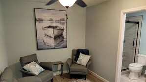 A living room with a grey sofa, a small table, a chair, a rug, and a painting of a boat on the wall. - Lou's Place @ COLE'S LODGE (Carrabelle)