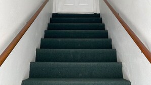 A staircase with dark carpeted steps, white walls, and a white door at the top. - Lou's Place @ COLE'S LODGE (Carrabelle)