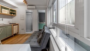 Ein kompakter Wohnbereich mit Küchenzeile, einer Couch, einem Bett und einem großen Fenster mit Blick auf die Stadt.