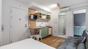 Ein kleines Hotelzimmer mit Bett, einer Küchenzeile, einer Dusche und einer Sitzecke.