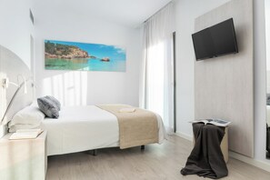 Une chambre d’hôtel avec un lit, une table de chevet sur laquelle se trouve un livre, un téléviseur fixé au mur et une fenêtre avec des rideaux.
