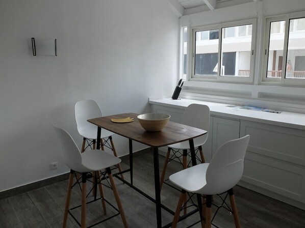 A dining area with a table and four chairs, a bowl on the table, and a window with a view of buildings.