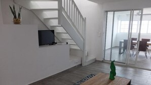 A modern living room with a staircase, a flat-screen TV, a wooden coffee table, and a dining area with a glass door. - Appartement de charme , Marina Royale, Marigot (Marigot)